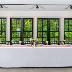 head table in front of tree lined windows at south haven creations venue