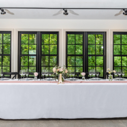 head table in front of tree lined windows at south haven creations venue